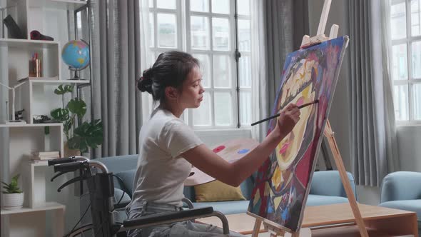 Asian Artist Girl In Wheelchair Holding Paintbrush Thinking And Painting A Girl On The Canvas