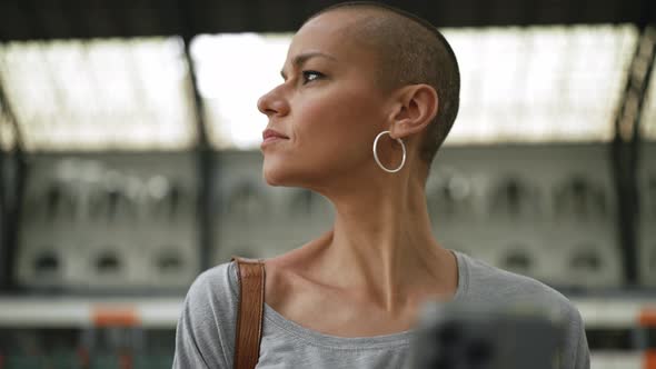 Worried bald woman wearing t-shirt typing by phone and looking around