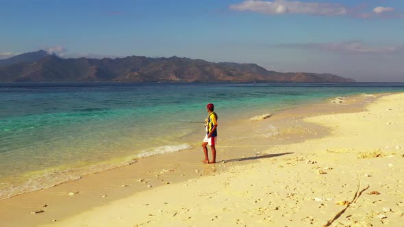 Guy fishing on beautiful lagoon beach break by blue ocean with white sand background of Gili Meno ne