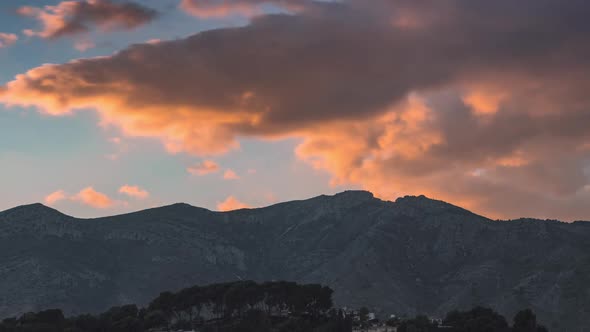 Timelapse of huge cloudsing fast over and behind a mountain during sunset