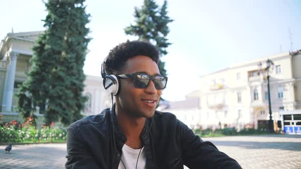 Portrait of Young Stylish Hipster Black Man in White Headphones and Sun Glasses Dancing Outdoor in