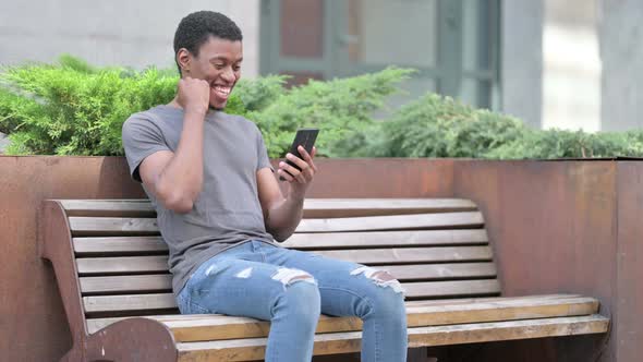 Ambitious Young African Man Celebrating Success on Smartphone