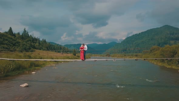 Сouple Stands on Bridge Over a Mountain River. Love of Man and a Woman