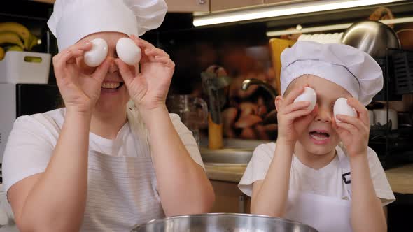 Happy Mother and Little Son Wearing Aprons Holding Eggs in Front of Eyes