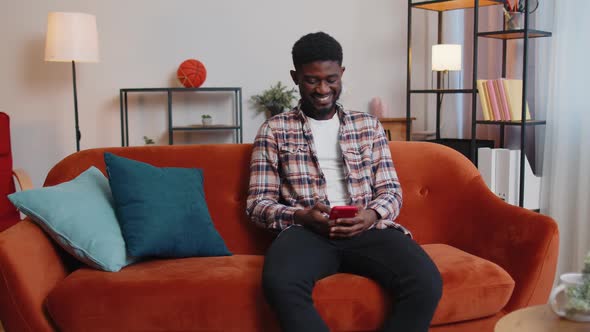 Cheerful Young Man Sitting on Sofa Using Mobile Phone Share Messages on Social Media Application