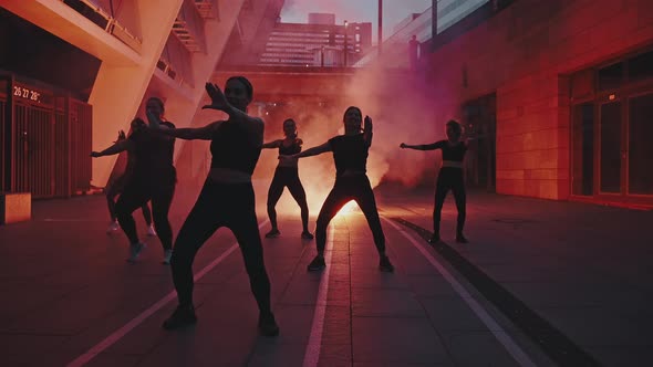 Silhouettes of Six Beautiful Girls Dancing at Night on a City Street Against the Background of a