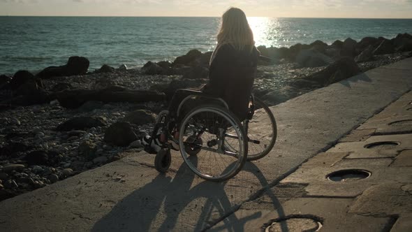 Young Lady with Disease of Spine Is Sitting in Wheelchair on Coast of Sea