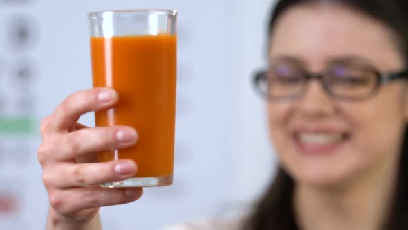 Smiling Woman in Eyeglasses Showing Fresh Carrot Juice, Vitamins for Eyes Health