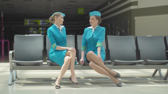Wide Shot of Young Beautiful Stewardess Calming Down Colleague in Airport Terminal. Tired Expert