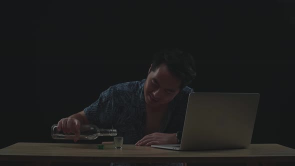 Drunk Asian Man Drinking Vodka During Having Video Call On A Laptop In Black Background