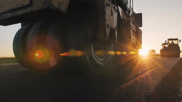 A Grunge Road Roller Levels the Asphalt in the Setting Sun. Road Surface Repair. Construction of a