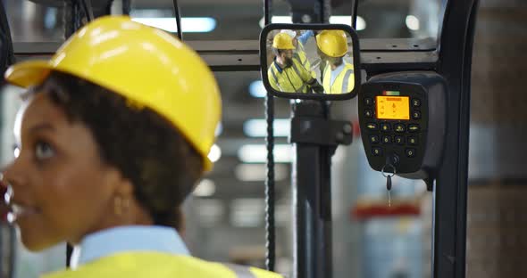 Female Forklift Driver Sitting in Truck and Talking to Colleagues Reflected in Rear View Mirror