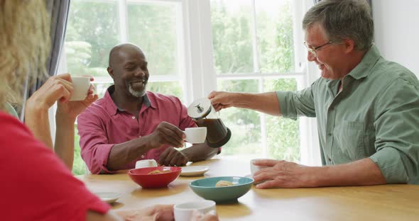 Animation of happy diverse female and male senior friends drinking coffee at home