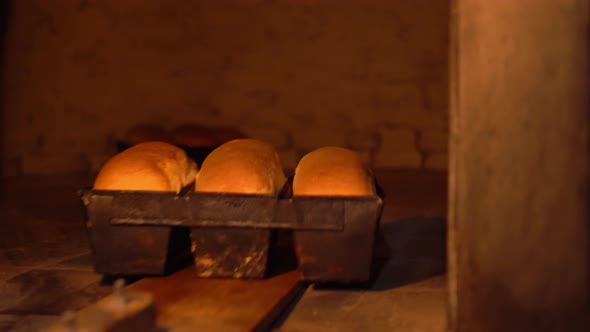 Baker takes bread out into oven with shovel.