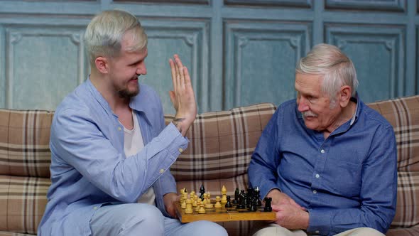 Happy Different Male Generations Family of Senior Father and Adult Son or Grandson Playing Chess