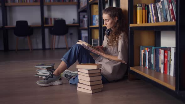 Thoughtful Female Student Sitting Against Bookshelf with a Books on the Floor