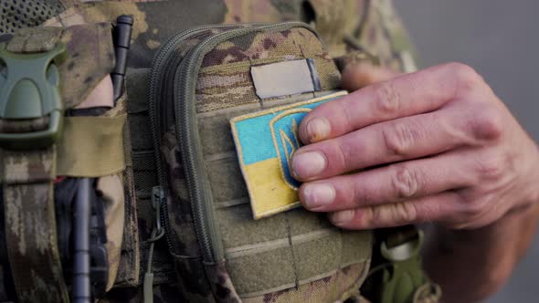 A Closeup of a Ukrainian Soldier in Military Uniform Who Sticks a Small Ukrainian Flag on His