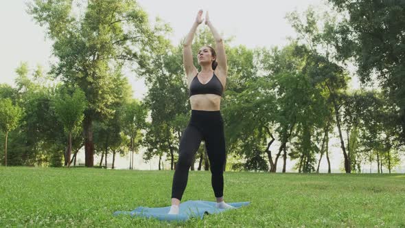 Young Fit Woman Practicing Warrior 1 Yoga in Park at Sunset