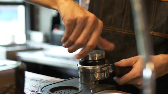 Close up Asian barista tamping powder of coffee on espresso machines shot.