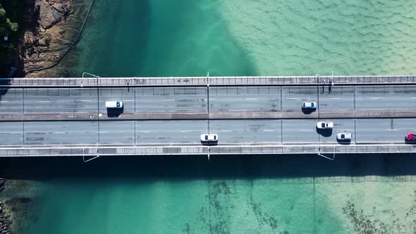 Busy coastal road and pedestrian bridge spanning a clear ocean estuary allowing people and vehicles