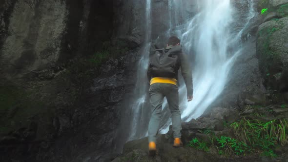 man with backpack on his back is walking alone to waterfall in depths jungle.