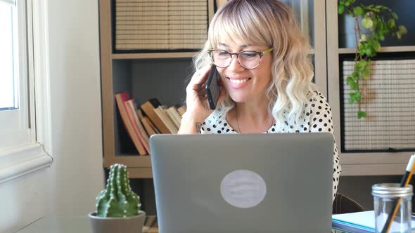 Blonde mature lady speaking with cellular for work at home - office desktop and female people call