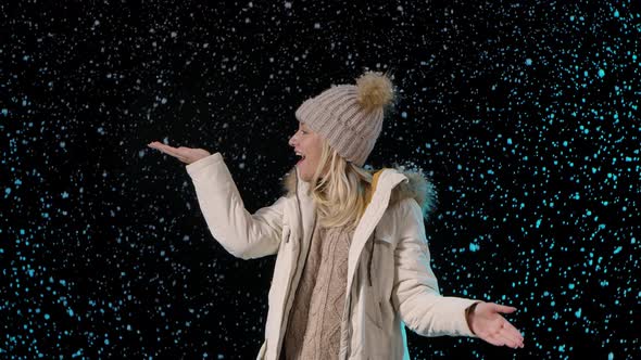 Portrait of a Young Woman Enjoying the Snowfall. A Blonde in Warm Winter Clothes on a Black