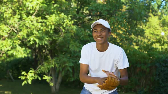 Happy Black Male Teenager Wearing White Cap Receiving and Throwing Baseball