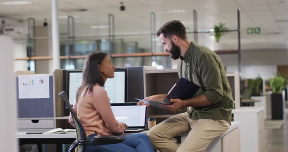 Video of diverse businesswoman and businessman using laptop and talking in office