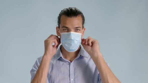 Front view shot of young man putting on hygienic mask. Static, bluish background