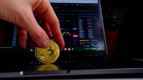 A bitcoin gold coin in hand on a laptop against the background of an open exchange program with cryp