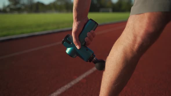 An Athlete Massages with a Percussion Therapy Gun to Relieve the Pain of Muscle Aches After a