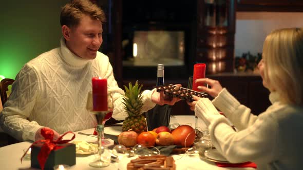 Smiling Loving Man Sharing Sweet Candies with Happy Woman Sitting at Valentine's Table Indoors at