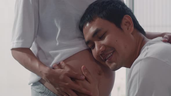 Young Asian Pregnant couple man kiss his wife belly talking with his child feeling happy smiling