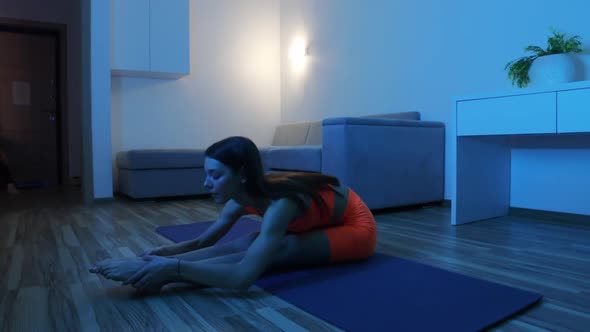 Fitness at Home in Blue Lighting  Young Woman Stretching to Her Feet