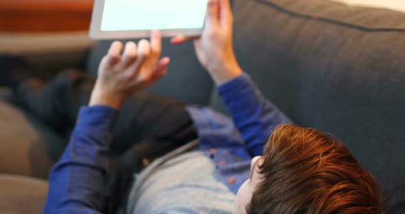 Man lying on sofa and using digital tablet in living room