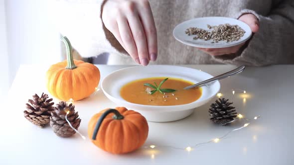 woman hand crumbles breadcrumbs into pumpkin soup