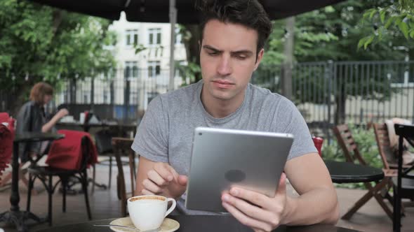 Man Drinking Coffee and Browsing on Tablet While Sitting in Cafe Terrace