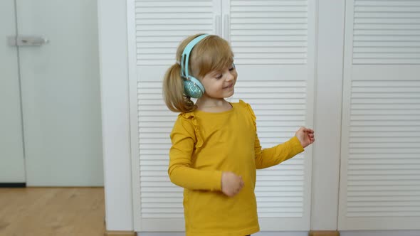 Little Child Girl Wearing Headphones Listening To Music and Funnily Dancing Near Wardrobe at Home