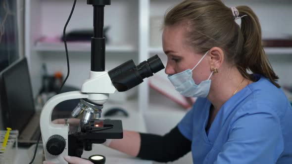 Side View Concentrated Caucasian Laborant Analyzing Blood Sample with Microscope in Slow Motion