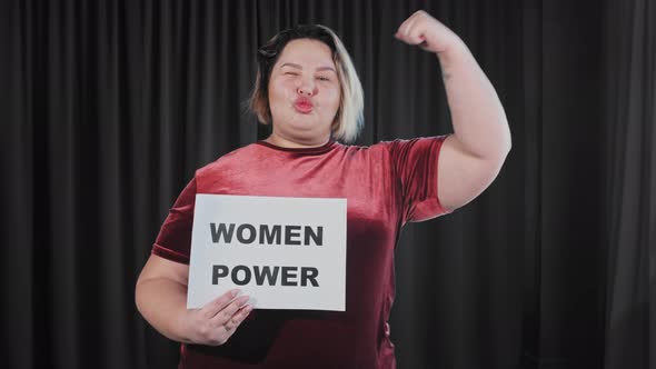 A Confident Flirty Overweight Woman Holding a Nameplate with a Sign WOMEN POWER