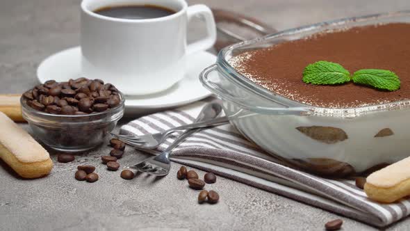 Tiramisu Dessert in Glass Baking Dish and Cup of Fresh Hot Espresso Coffee on Concrete Background