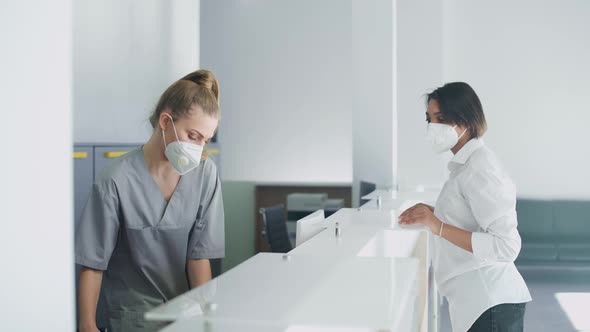 Hospital Reception a Nurse Registers an Young Woman Patient for a Doctor's Appointment in a Modern