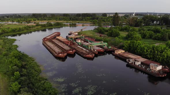 Aerial View of Large Rusty Barges in a Port on the River Bank Among Green Fields and Forests. Slow