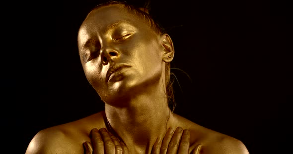 Portrait of a Girl with Golden Glowing Skin on a Black Background. She Closes Her Eyes, Stroking Her