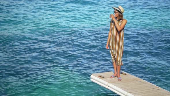 A woman with a glass of white wine on a dock over the Mediterranean Sea in Italy, Europe