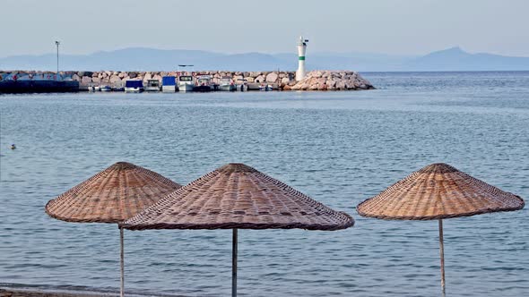 Straw Umbrellas On The Beach And People Swimming In The Sea