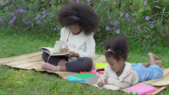 Happy African family with children lying reading or writing to book in the garden.