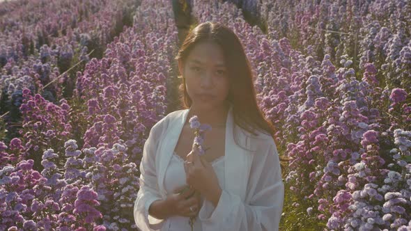 Young Asian Woman in Flower Field on Sunset Look at Camera