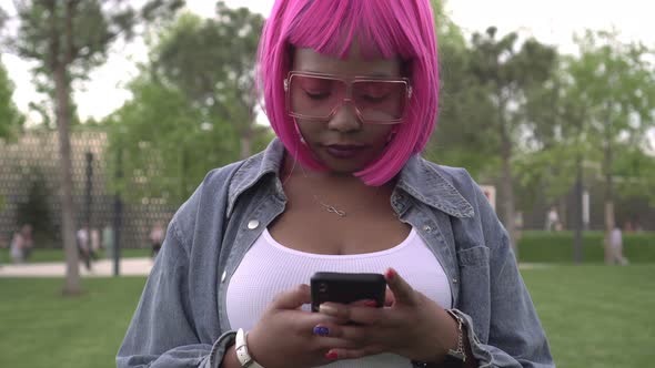 Young Attractive Black African Woman with Big Breasts Uses a Smartphone